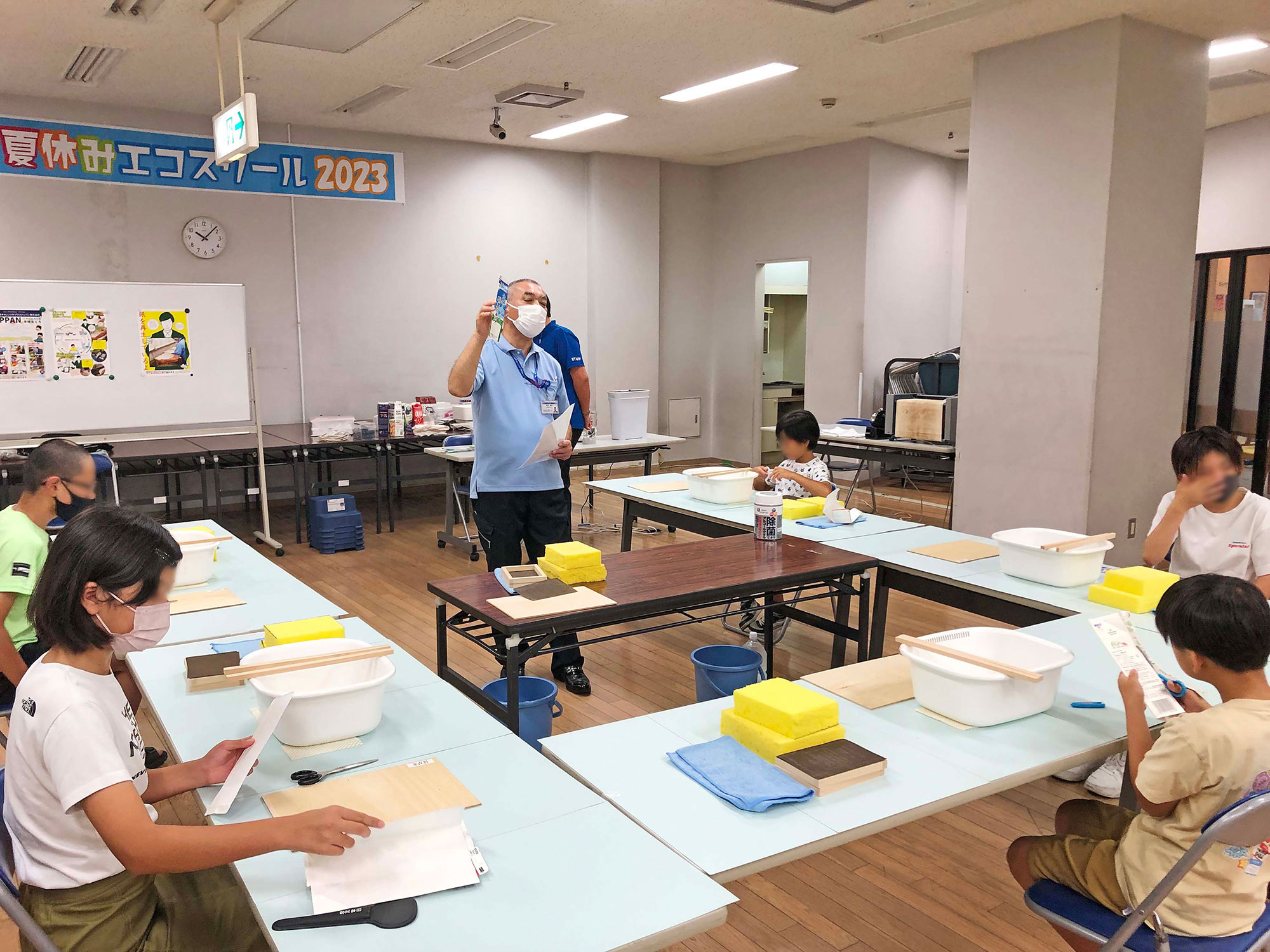 2023年エコポリス紙すきイベント会場で子供達にスタッフが説明している写真