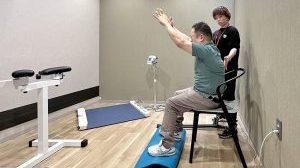 パーソナルサポートの様子。椅子に座った状態で手を上に伸ばす社員と、その背中に手を添える専門スタッフ。